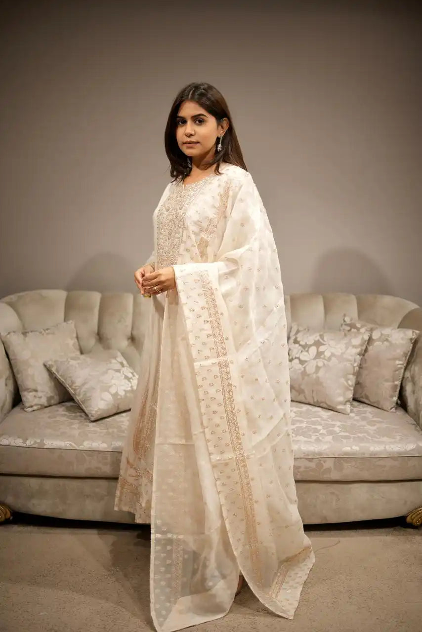 Woman in a white traditional outfit standing in a room with a beige sofa and decorative pillows.