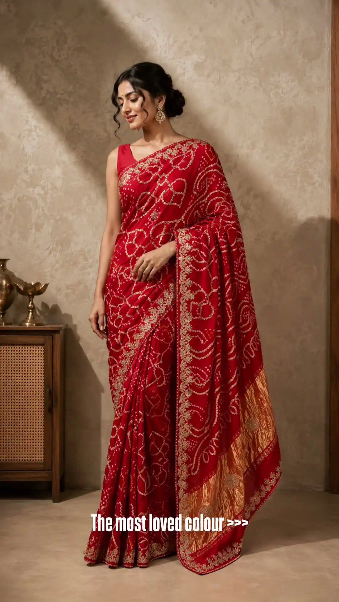 Woman wearing a red saree with gold patterns against a beige wall.