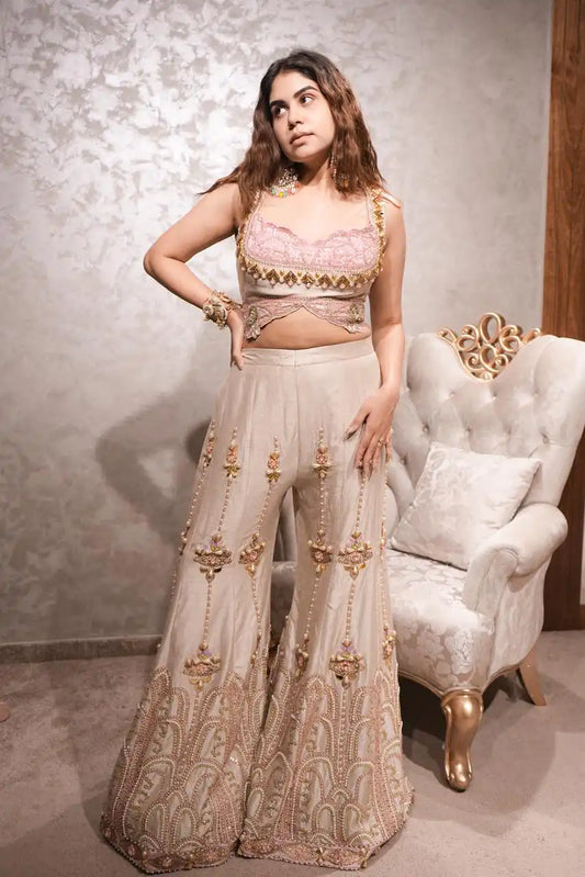 Woman in traditional outfit posing in a room with a decorative chair.
