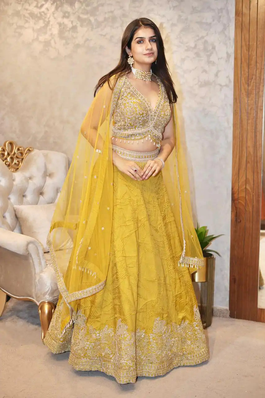 Woman in a yellow traditional outfit with intricate designs in an indoor setting.